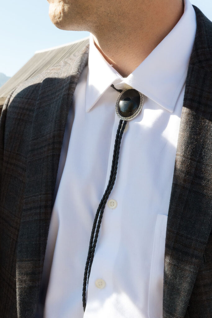 A man wearing a black bolo tie and grey suit jacket